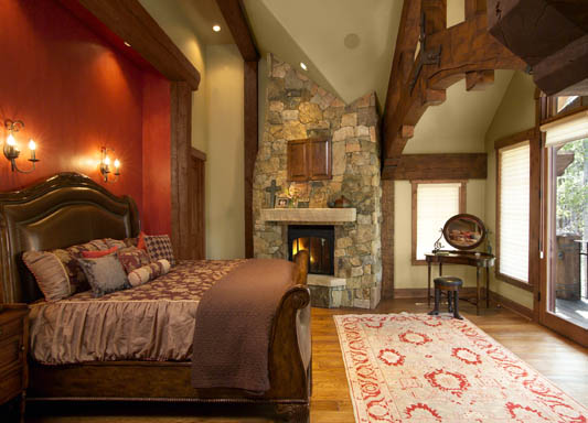 Master bedroom with a large timber truss and natural stone fireplace