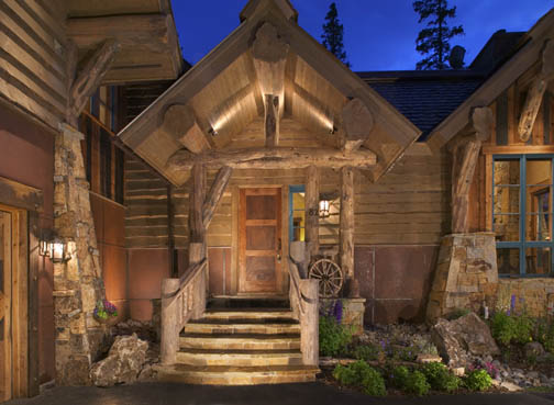 A very inviting entrance featuring log railings, flared cedar log butts, character log truss and log braces, natural stone and wood siding.